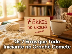 Mesa de trabalho de crochê com projeto inacabado em fio creme, agulhas de crochê, novelo de lã e xícara de chá. Ao centro, pequena placa com texto manuscrito "7 ERROS DO CROCHÊ". Iluminação natural suave, ambiente acolhedor e convidativo para aprendizado.
